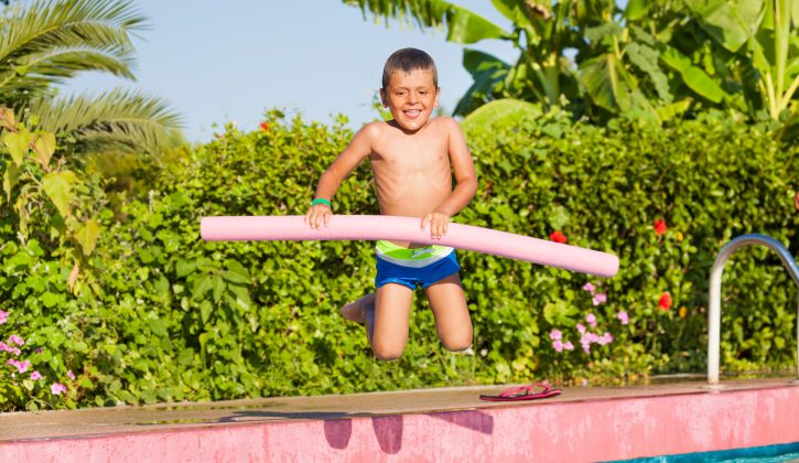 Jumping small boy holding inflatable ring standing near the swimming pool outside in summer