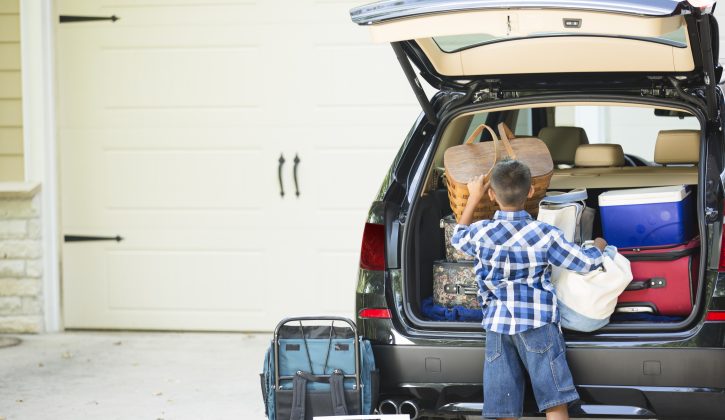 Family packs their vehicle for summer vacation.  One excited little boy waits by the car.