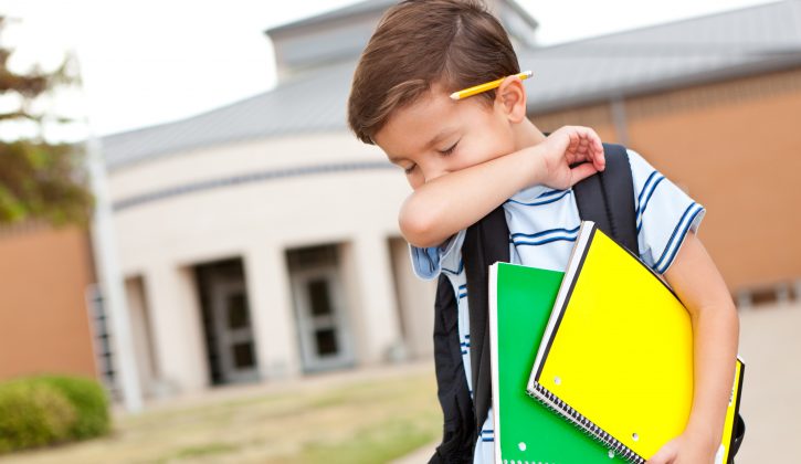 Young boy at school coughing into his arm.