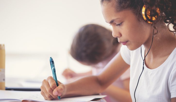 Young Aboriginal girls studying with headphones. They are working at a table at home. One girls listening to music or educational work as she works. They are sisters doing schoolwork together.