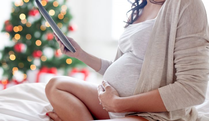 pregnancy, holidays, technology, people and expectation concept - close up of pregnant woman with tablet pc computer in bed at home over christmas tree background