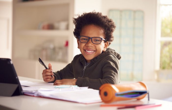 Portrait Of Boy Sitting At Kitchen Counter Doing Homework Using Digital Tablet