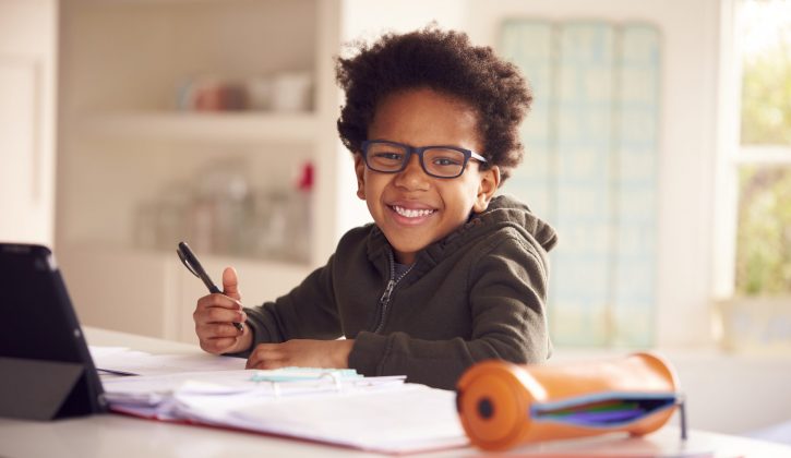 Portrait Of Boy Sitting At Kitchen Counter Doing Homework Using Digital Tablet