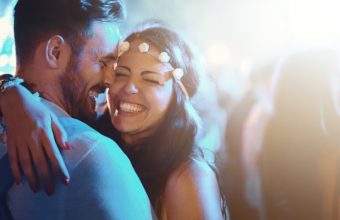 Closeup of late 20's couple on a date during an open air concert. They are having amazing time together with big crowd around them. Back lit.